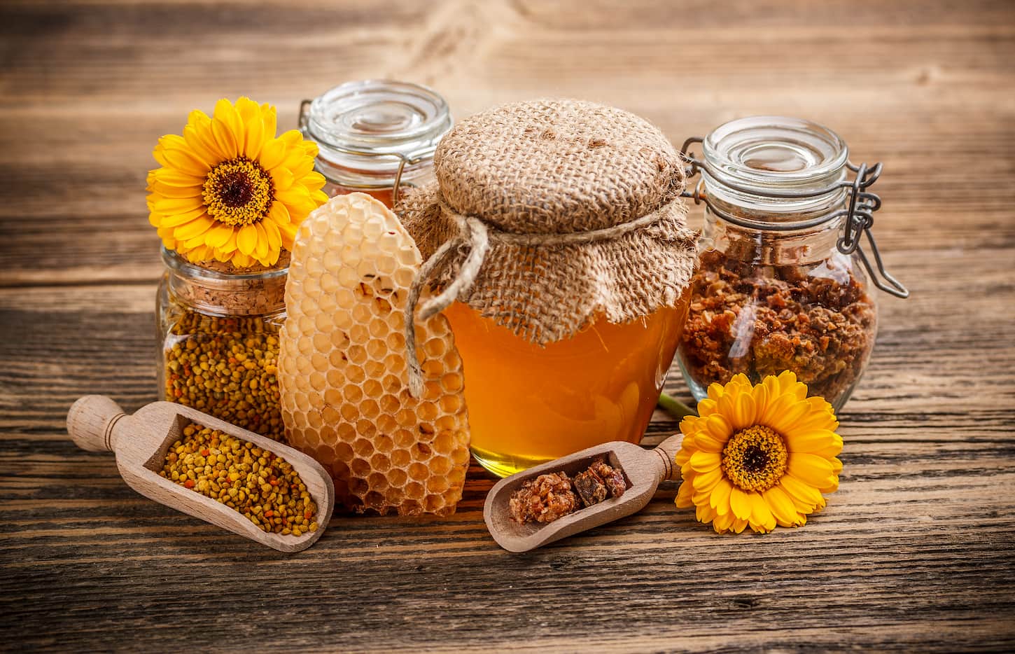 An image of some products that can be made out of honey beautifully arranged with sunflower embellishes on a wooden table.