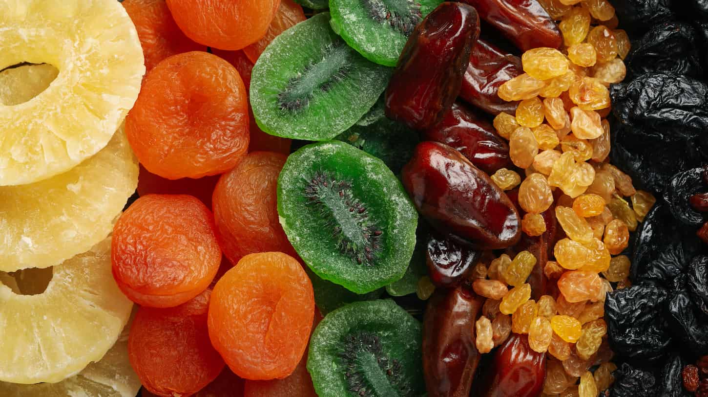 An image of different dried fruits and nuts on the whole background such as pineapples, apricots, kiwis, dates, raisins, and prunes.