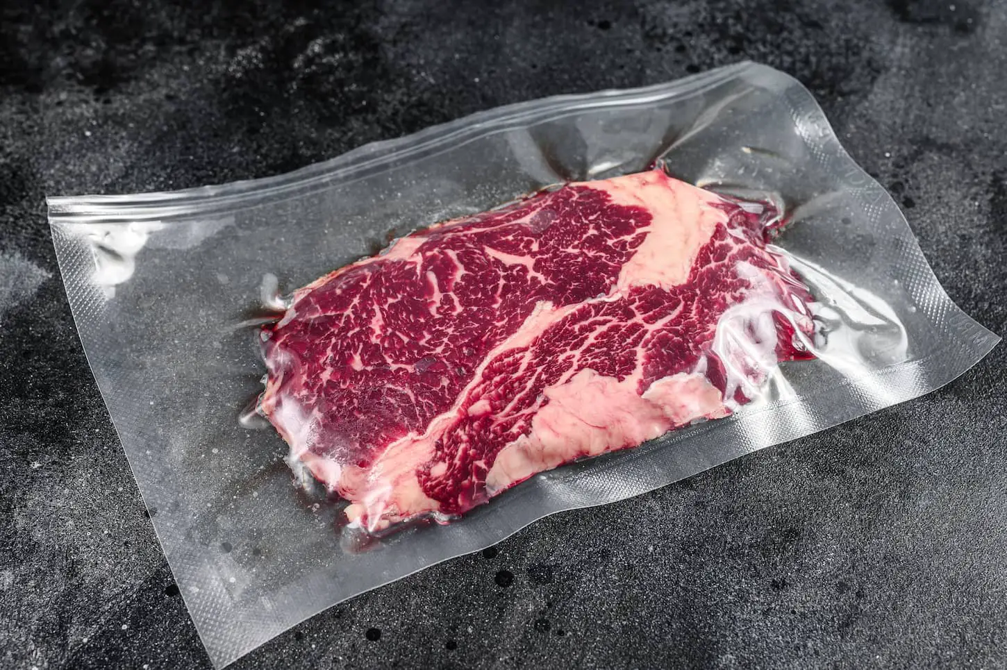 An image of raw rib-eye beef meat steak in vacuum packaging with black background.