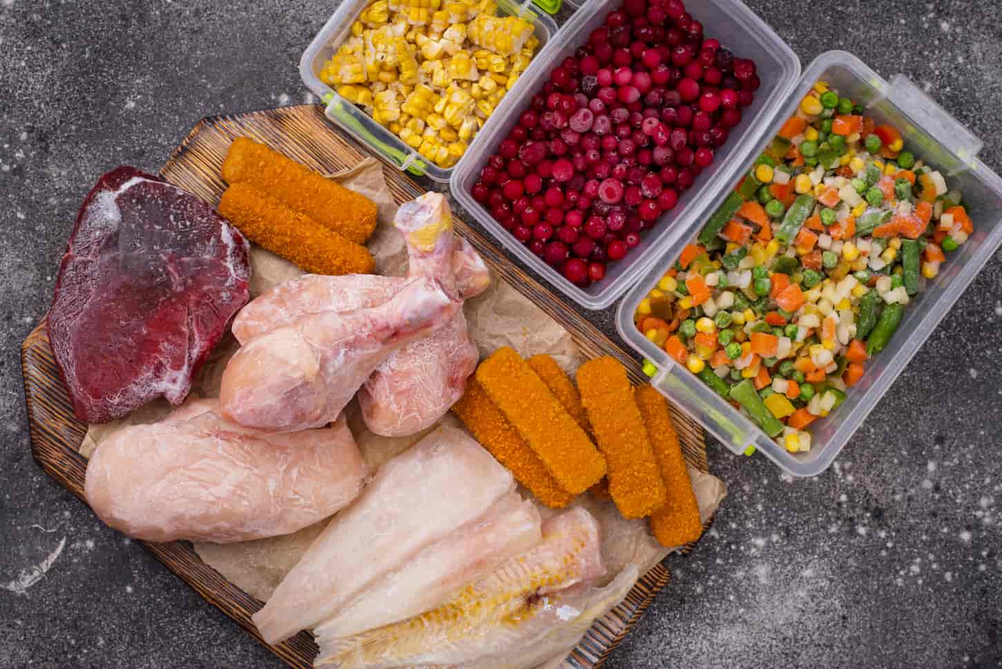 An image of various frozen vegetable products in containers, and various frozen meat in a wooden chopping board.