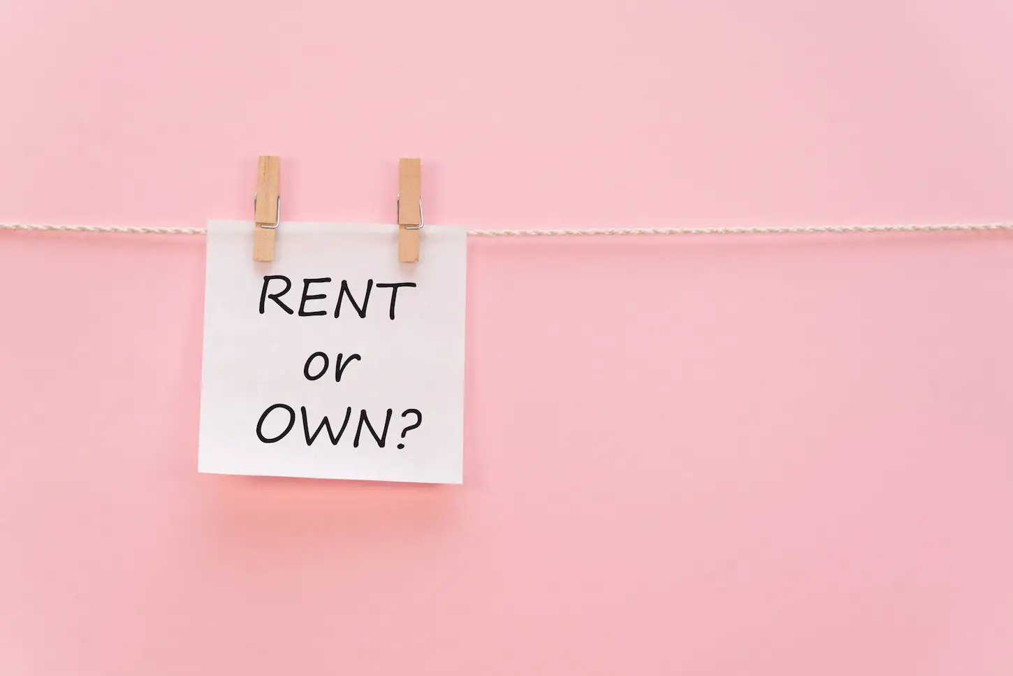 An image of a sticker with the inscription RENT or OWN hangs with a clothespin on a rope on a pink background.
