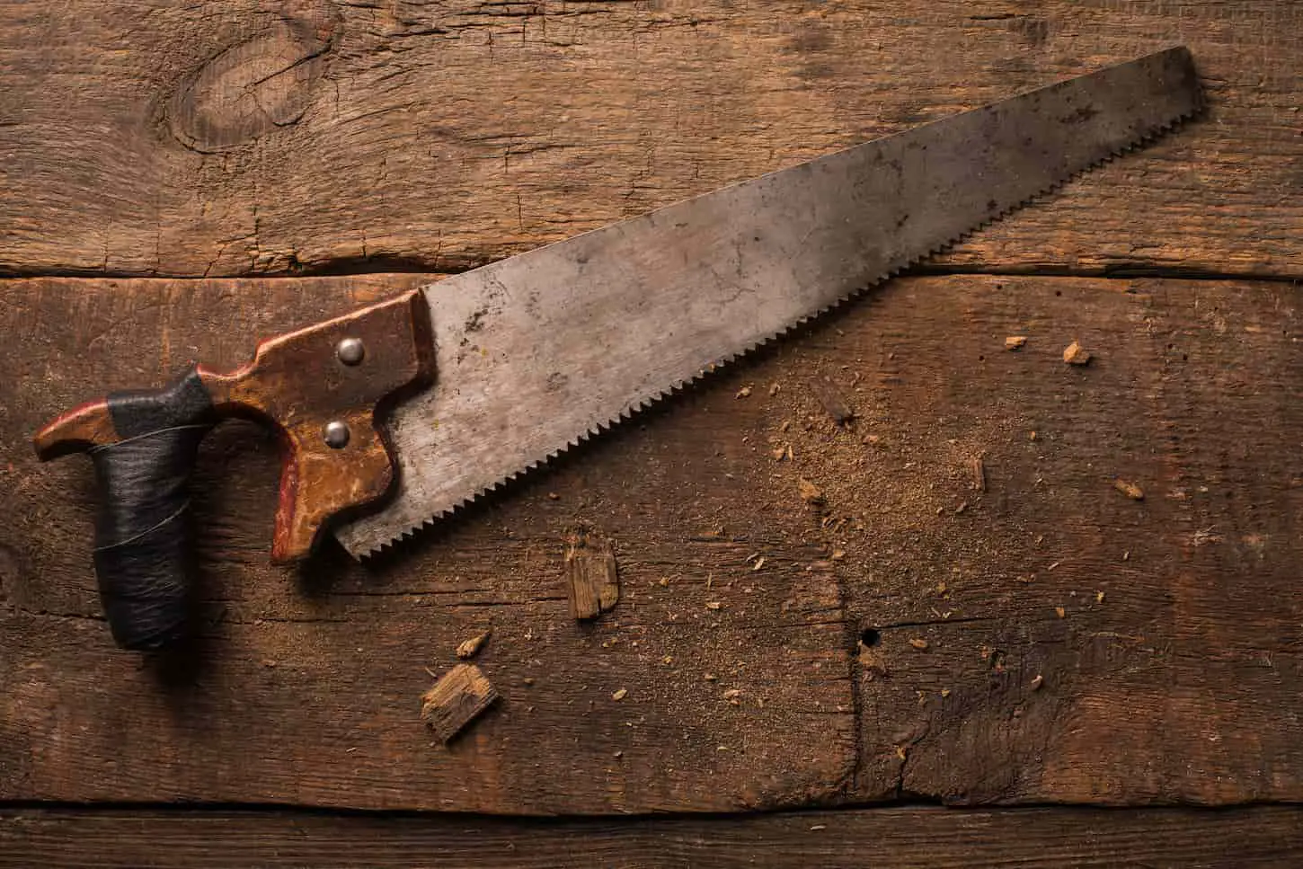 An image of a carpenter's rusty handsaw on a wooden table.