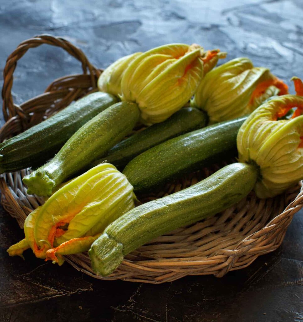 An image of zucchini with flowers in a basket on a dark background.