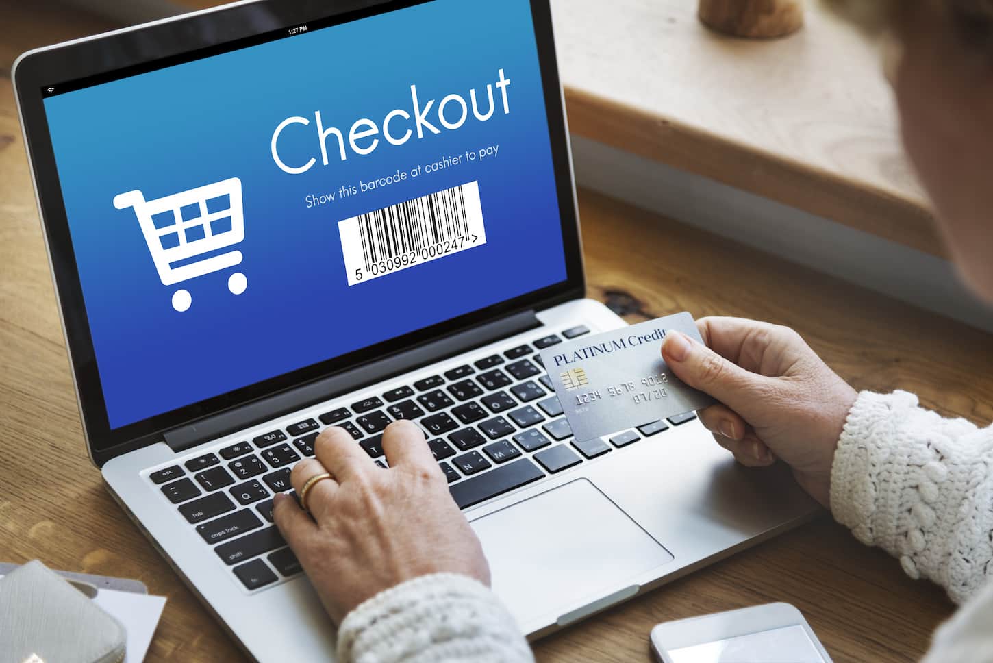 An image of a person holding a credit card in front of a laptop checking out an online purchase.