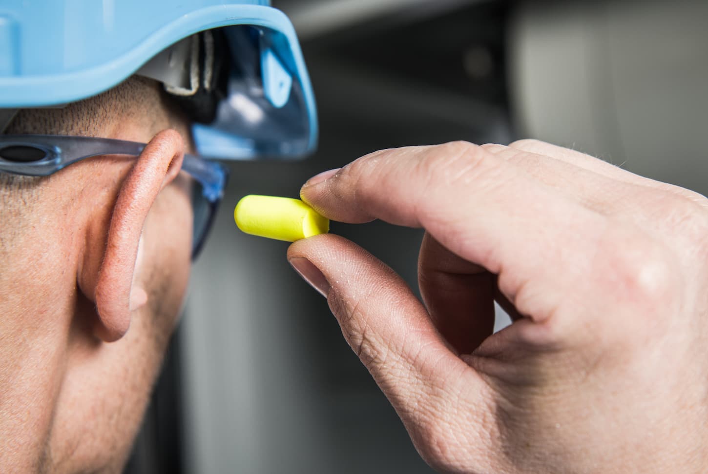 An image of a man with a hard hat and goggles putting earplugs for hearing protection rear view.