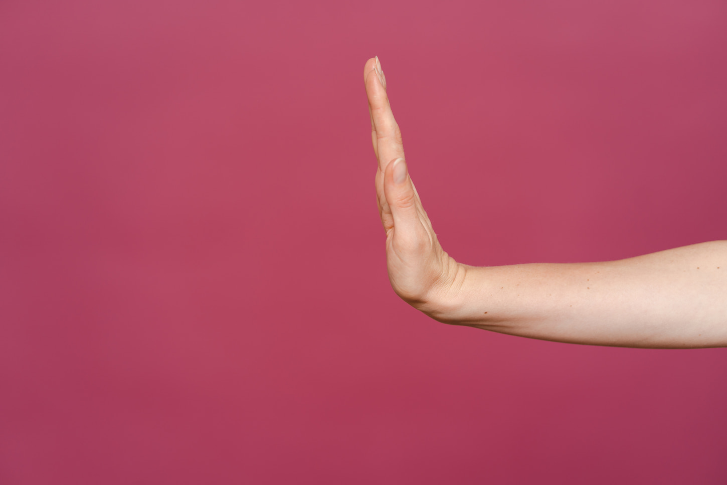 An image of a woman's hand showing stop sign on a pink background.