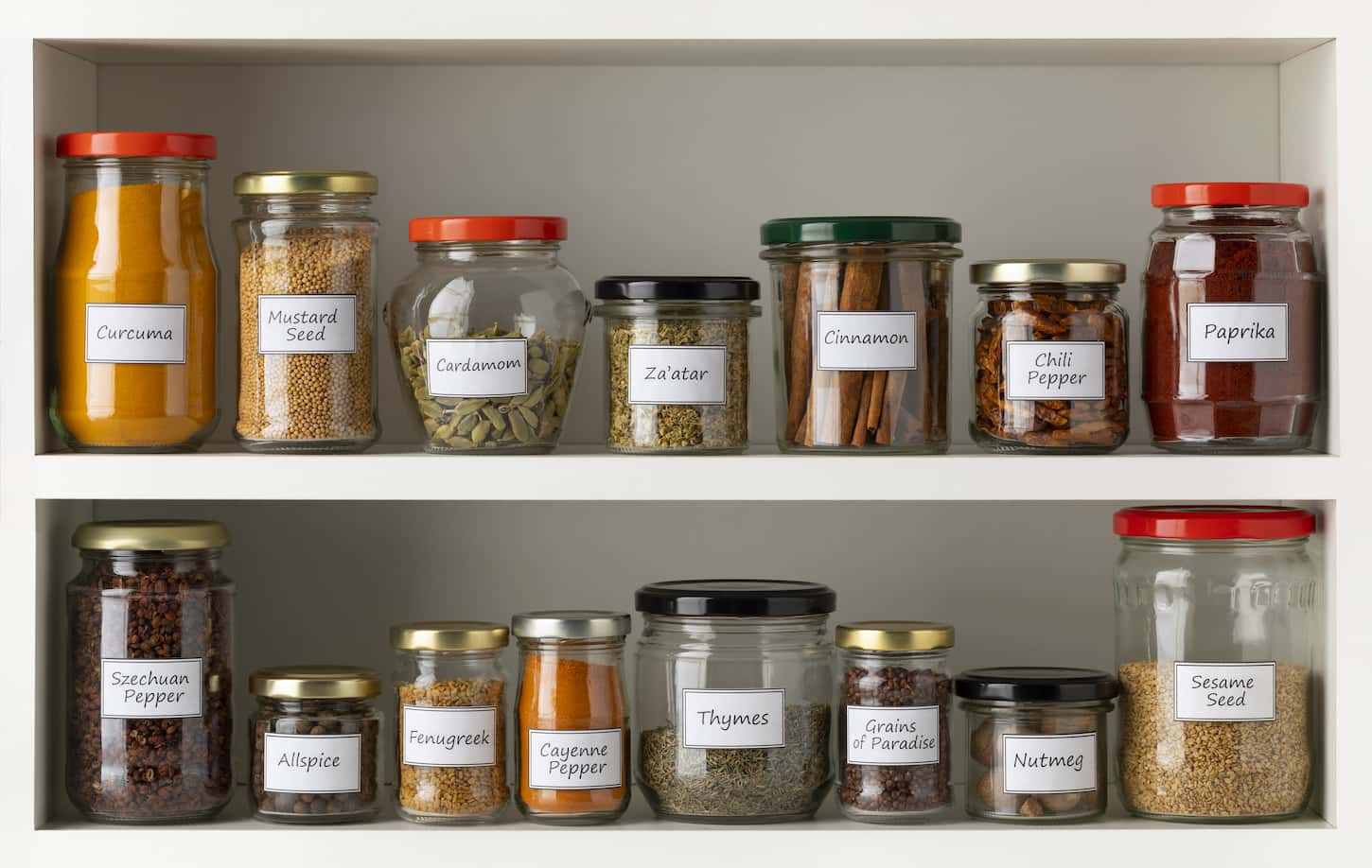 An image of recycled glass jars with a variety of dried herbs in a row on the kitchen shelf.